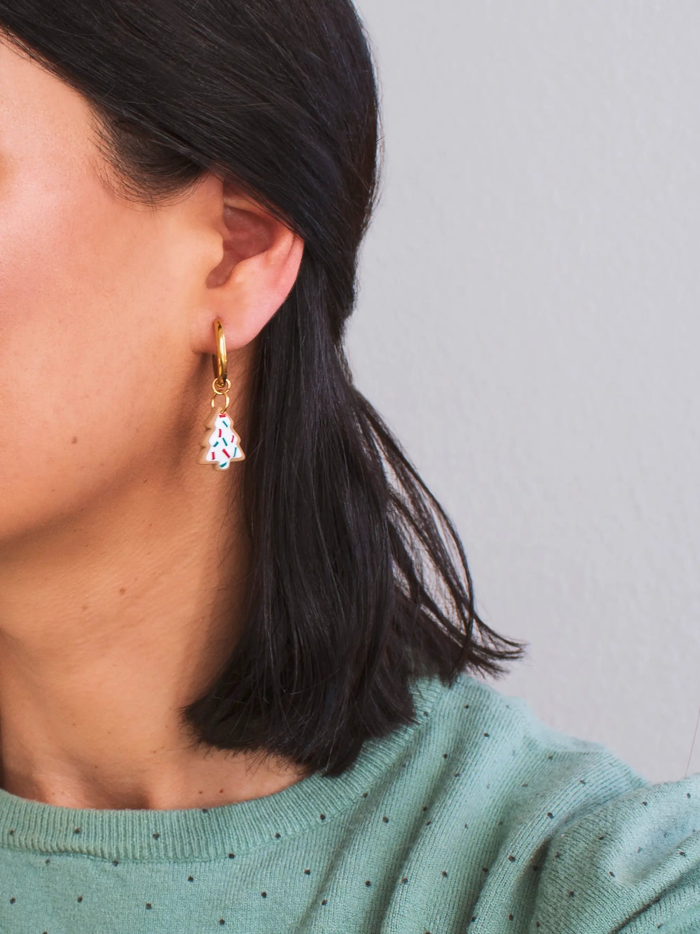 Close-up of Christmas charm hoop earring worn – Showcasing a Christmas tree charm made of handmade polymer clay with hypoallergenic gold-plated hoops.