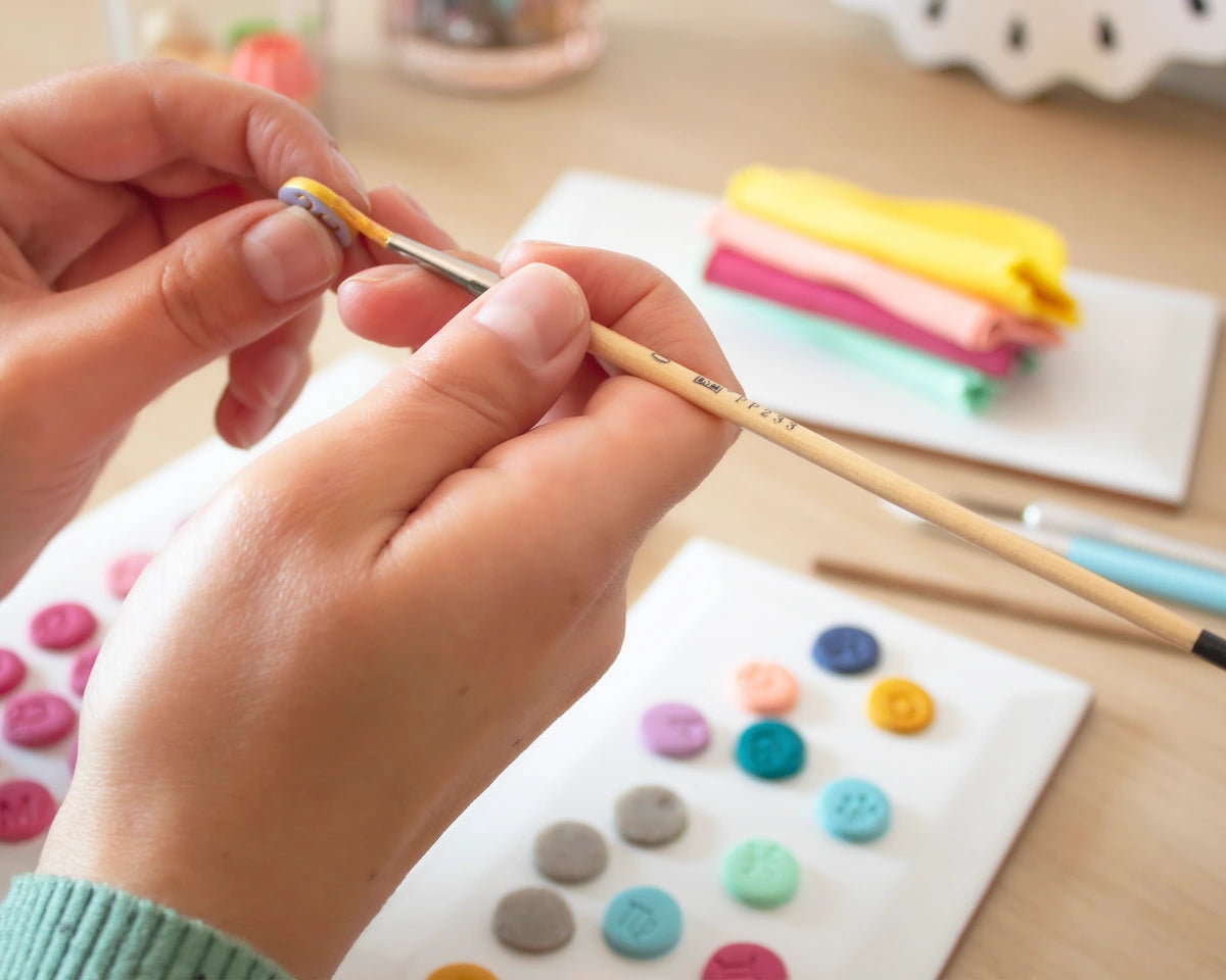Handcrafting clay charms in a jewelry studio, painting handmade colorful initials for Mariquilla Sandía