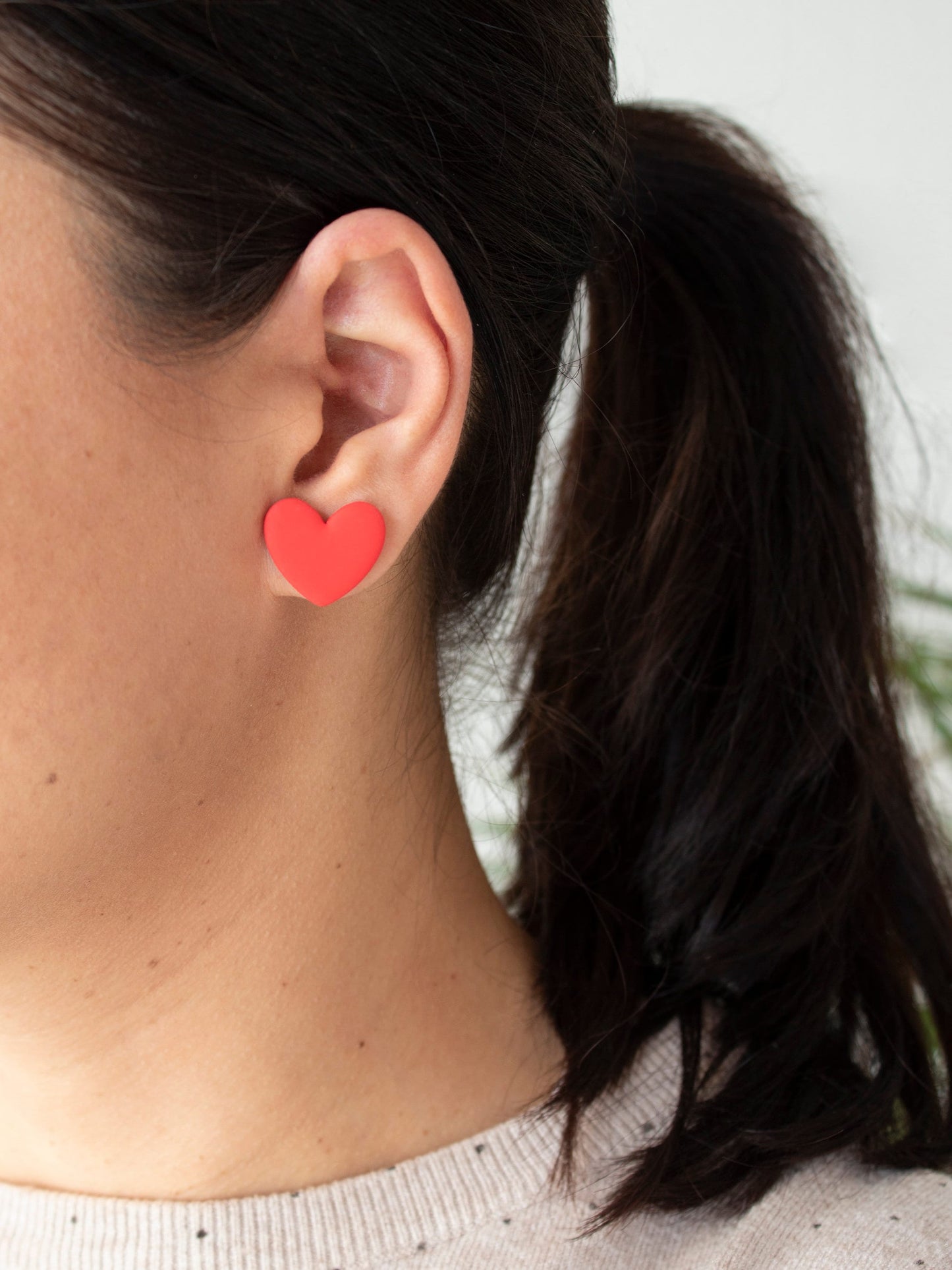 Model with red heart-shaped stud earrings. Handmade large earrings with heart shape, available colors: red, pink and sparkle.