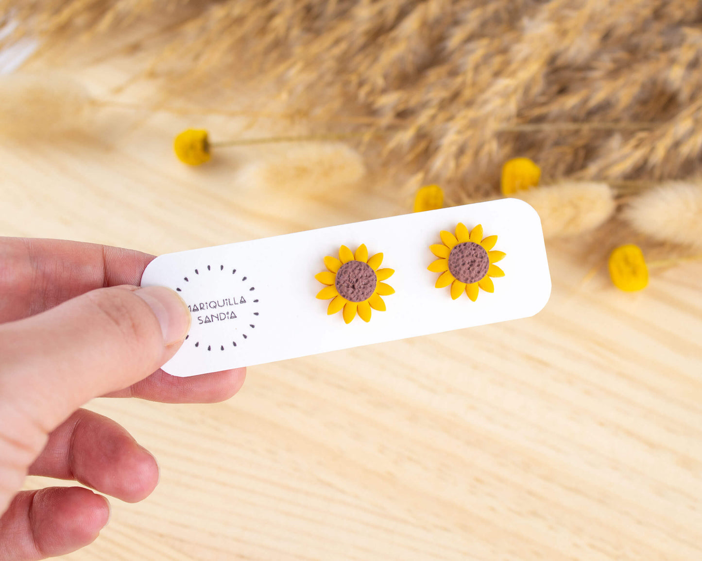 Handmade sunflower stud earrings displayed on a branded card, made from lightweight hypoallergenic clay.