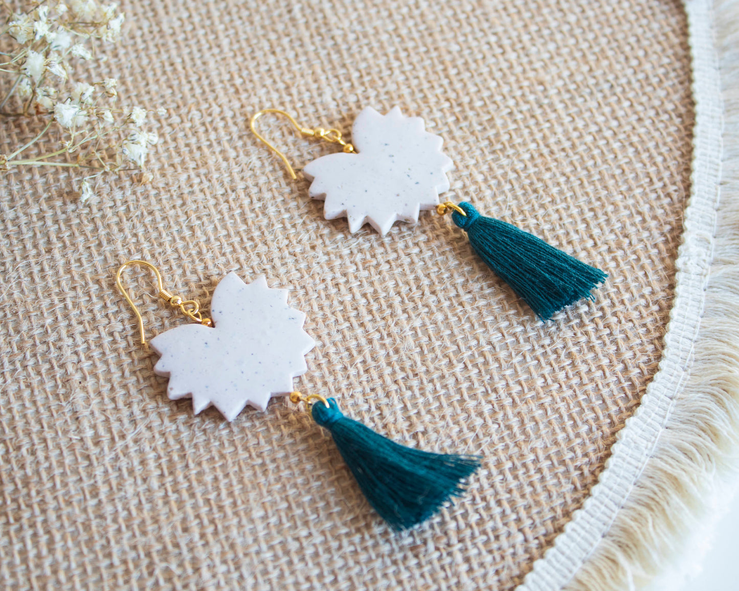 Handmade clay earrings with tassels, cream color, laid on a woven mat.