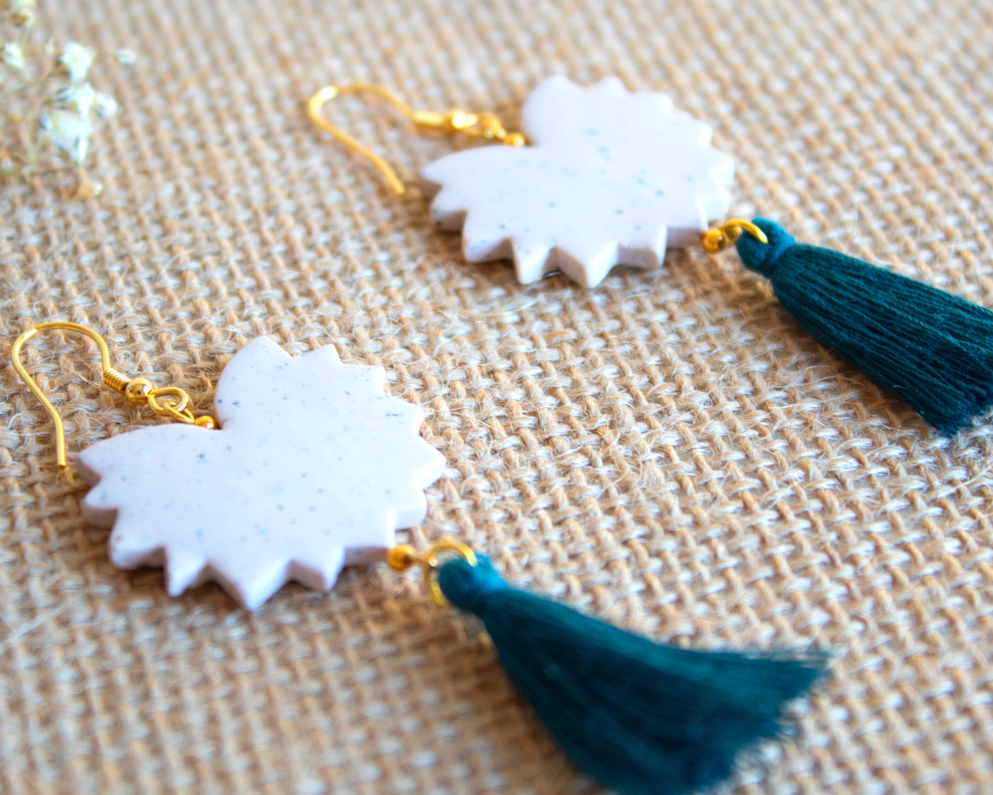 Handmade clay earrings with tassels displayed on a natural fabric, showcasing intricate details.