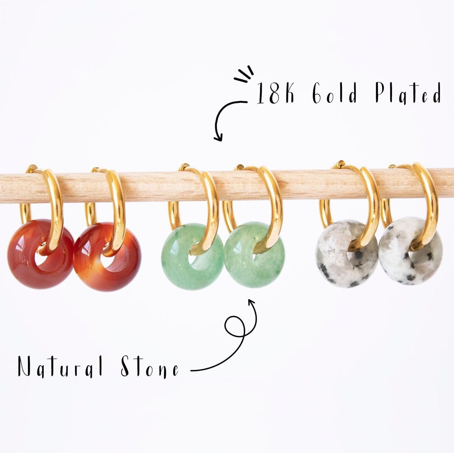 Gold hoop earrings with donut gemstone charms in Aventurine, Carnelian, and Dalmatian Jasper, displayed on a wooden rod