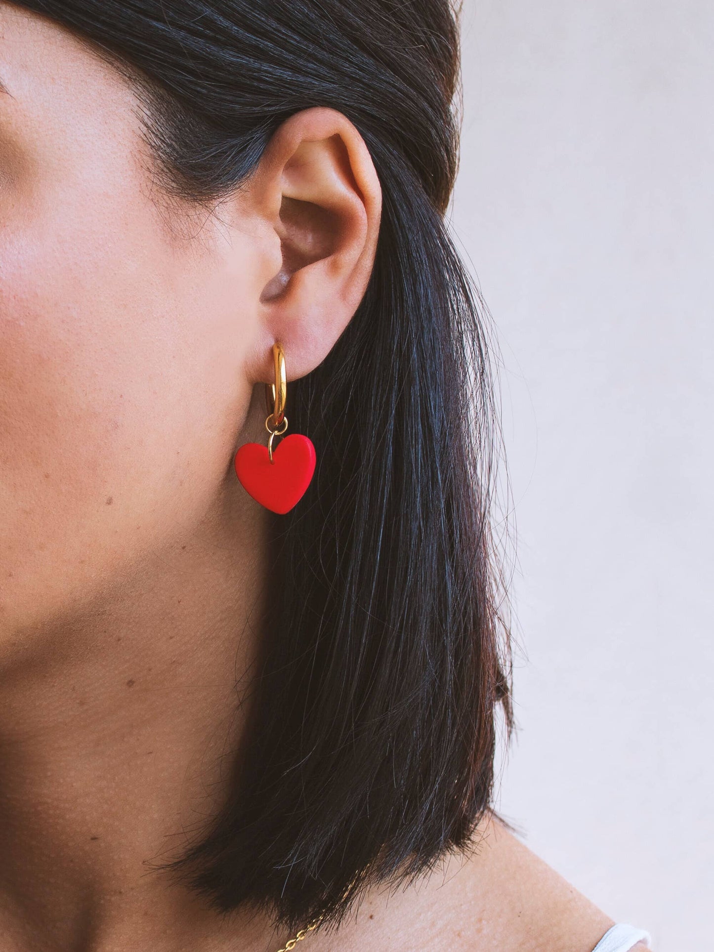 Red heart charm hoop earring worn by a model, featuring 18K gold plated hoops.