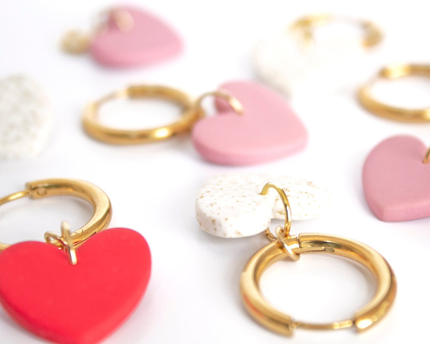 Close-up of mix-and-match heart charm hoop earrings, handmade with clay and gold-plated hoops.