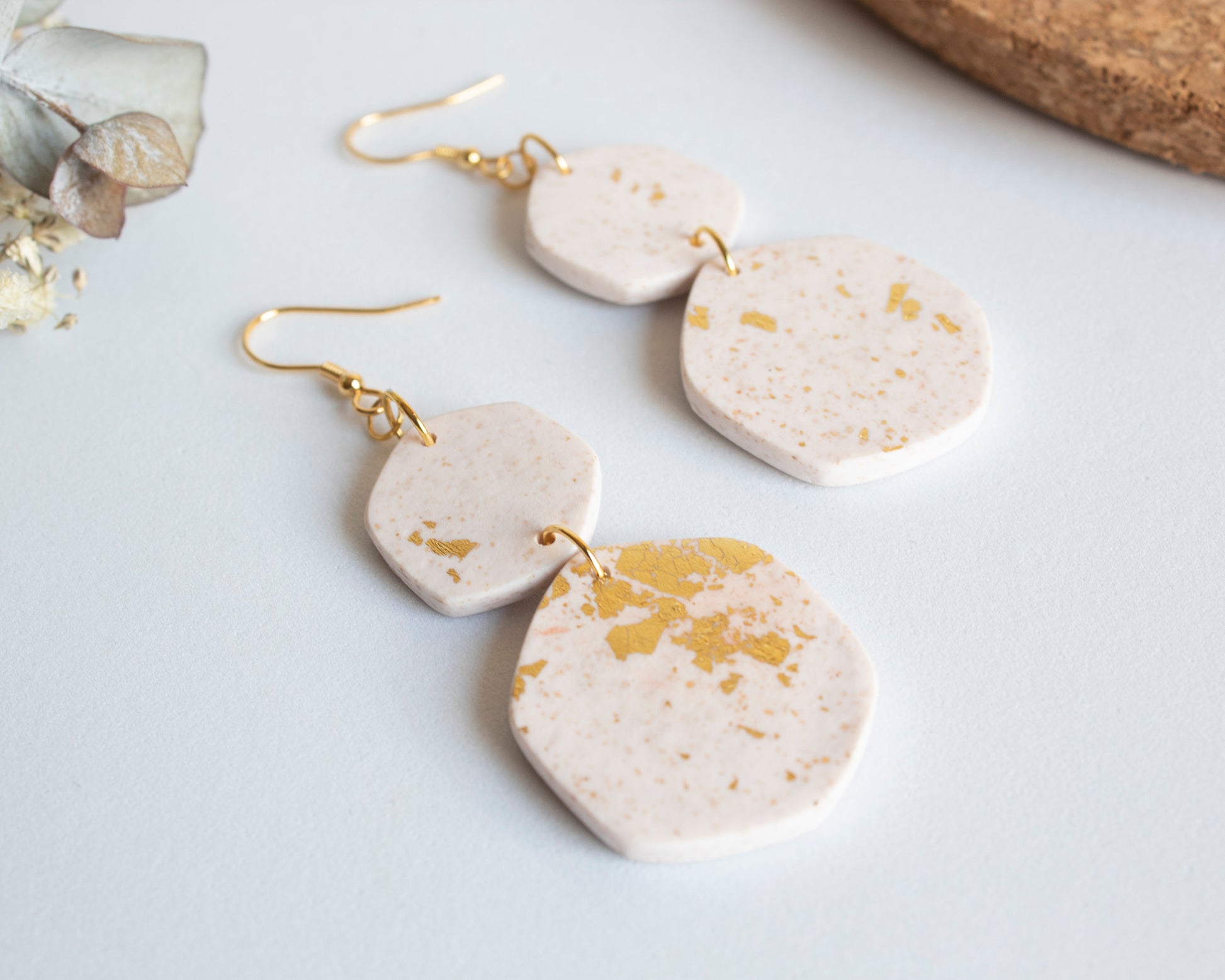 Detail shot of white and gold leaf boho earrings laid flat, showcasing the handcrafted geometric shapes and texture.