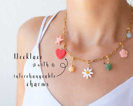 Close-up of a personalized necklace with interchangeable charms including initials, flowers, fruits and natural stones, displayed on a jewelry bust