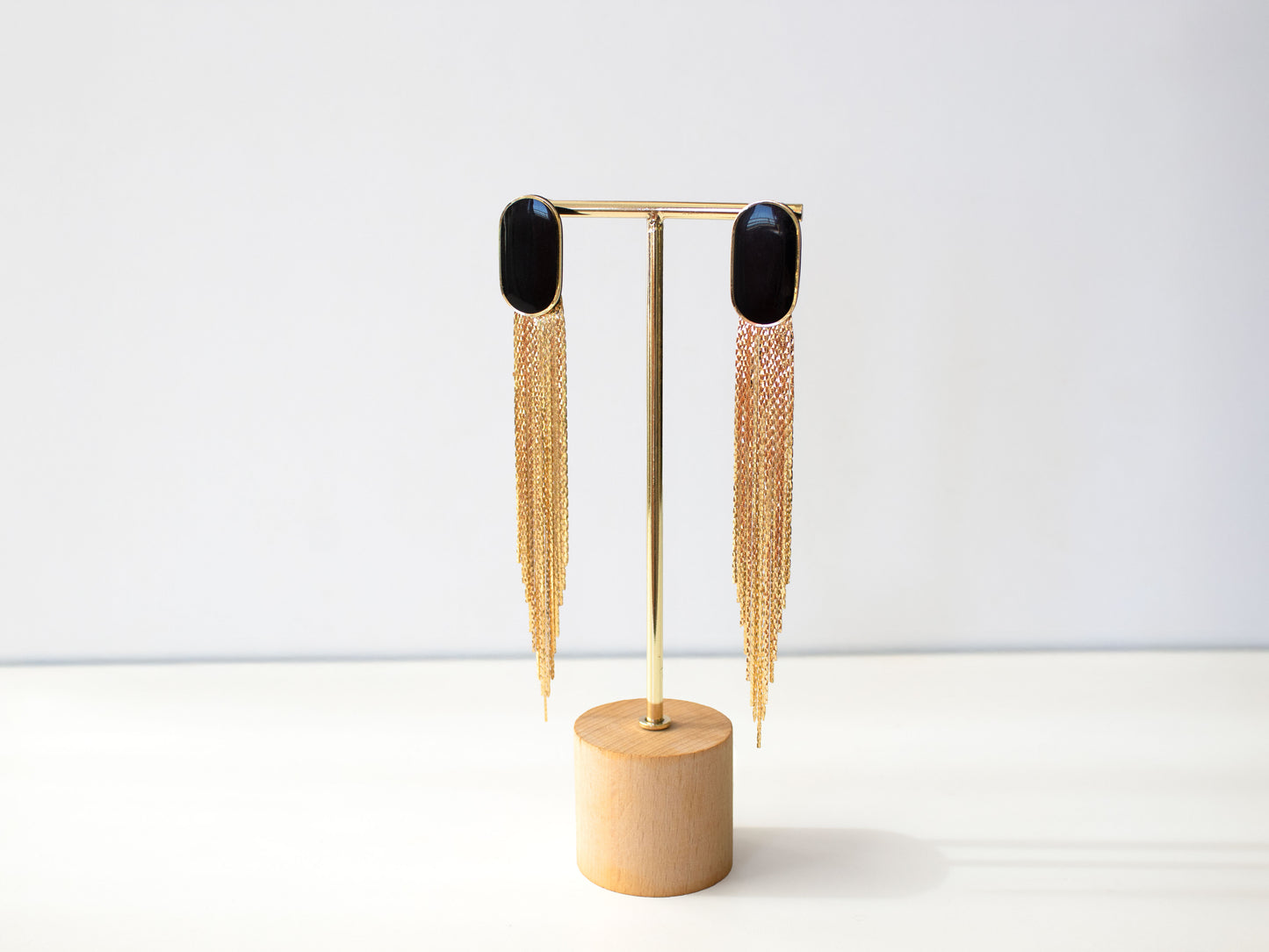 Extra long black and gold statement earrings hanging on stand