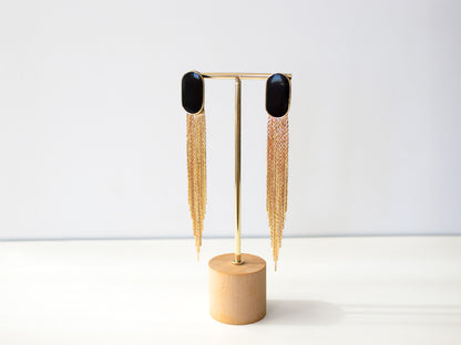 Extra long black and gold statement earrings hanging on stand