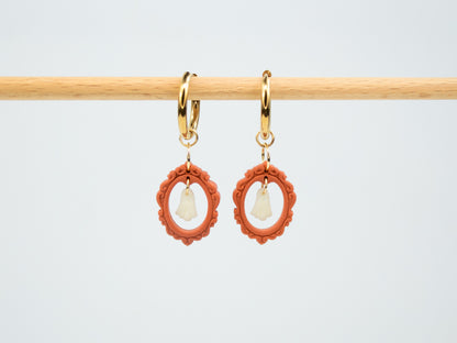 Spooky glow-in-the-dark ghost pendants in red vintage frames hanging from hoop earrings in the dark.