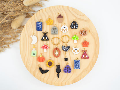 Handmade Halloween charm hoop earrings collection featuring interchangeable spooky and fall pendants like skull, pumpkin, mushroom, sunflower, witchy tarot, and glow-in-the-dark ghost.