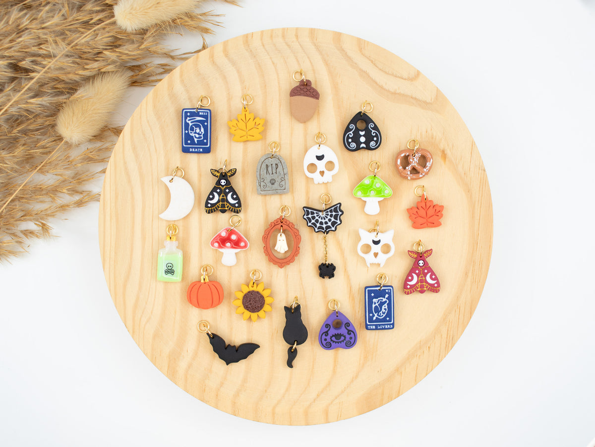 Assortment of handmade witchy fall jewelry charms including skulls, tarot cards, and pumpkins for interchangeable hoop earrings.