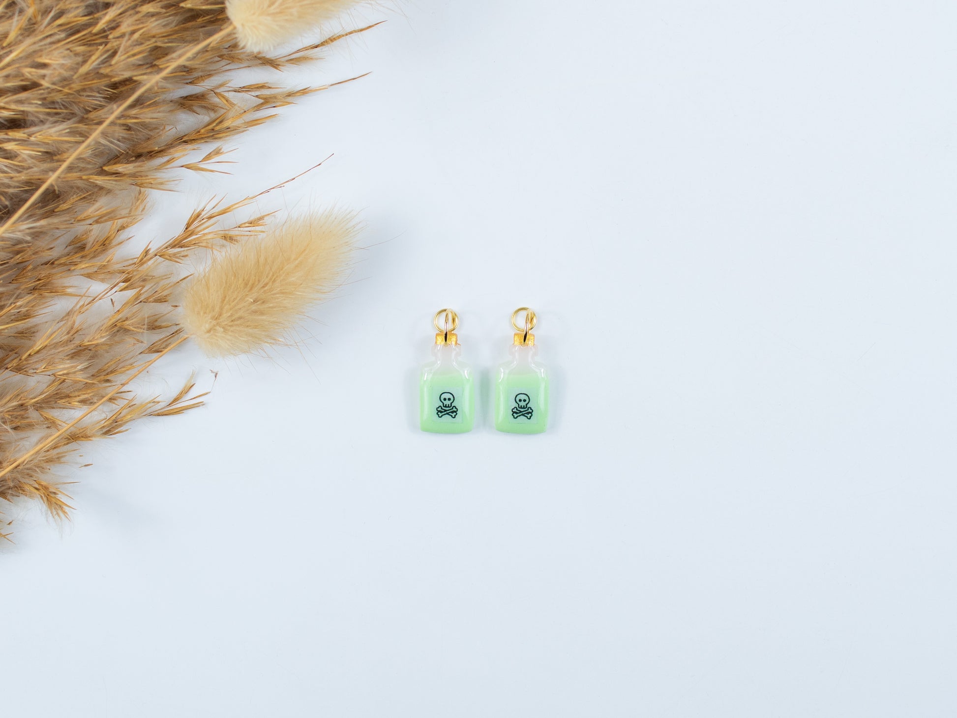 Spooky glow-in-the-dark poison bottle charms with skull and crossbones hanging from hoops in the dark.