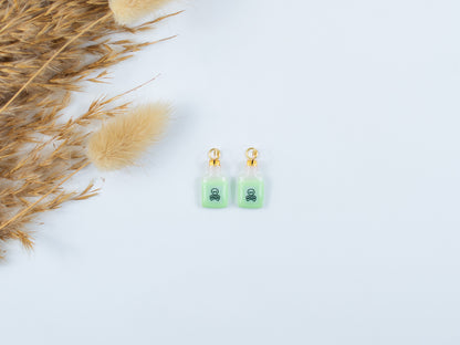 Spooky glow-in-the-dark poison bottle charms with skull and crossbones hanging from hoops in the dark.