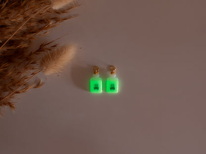 Handmade witchy potion bottle charm hoop earrings in pastel green with spooky skull and crossbones details.