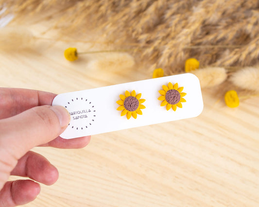 Handmade sunflower stud earrings displayed on a branded card, made from lightweight hypoallergenic clay.