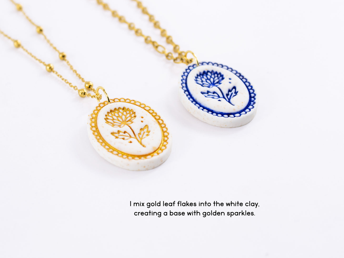 Close up of two birthflower gift pendants showcasing the white polymer clay base mixed with gold leaf flakes. One has a hand-painted blue flower and the other a gold flower.