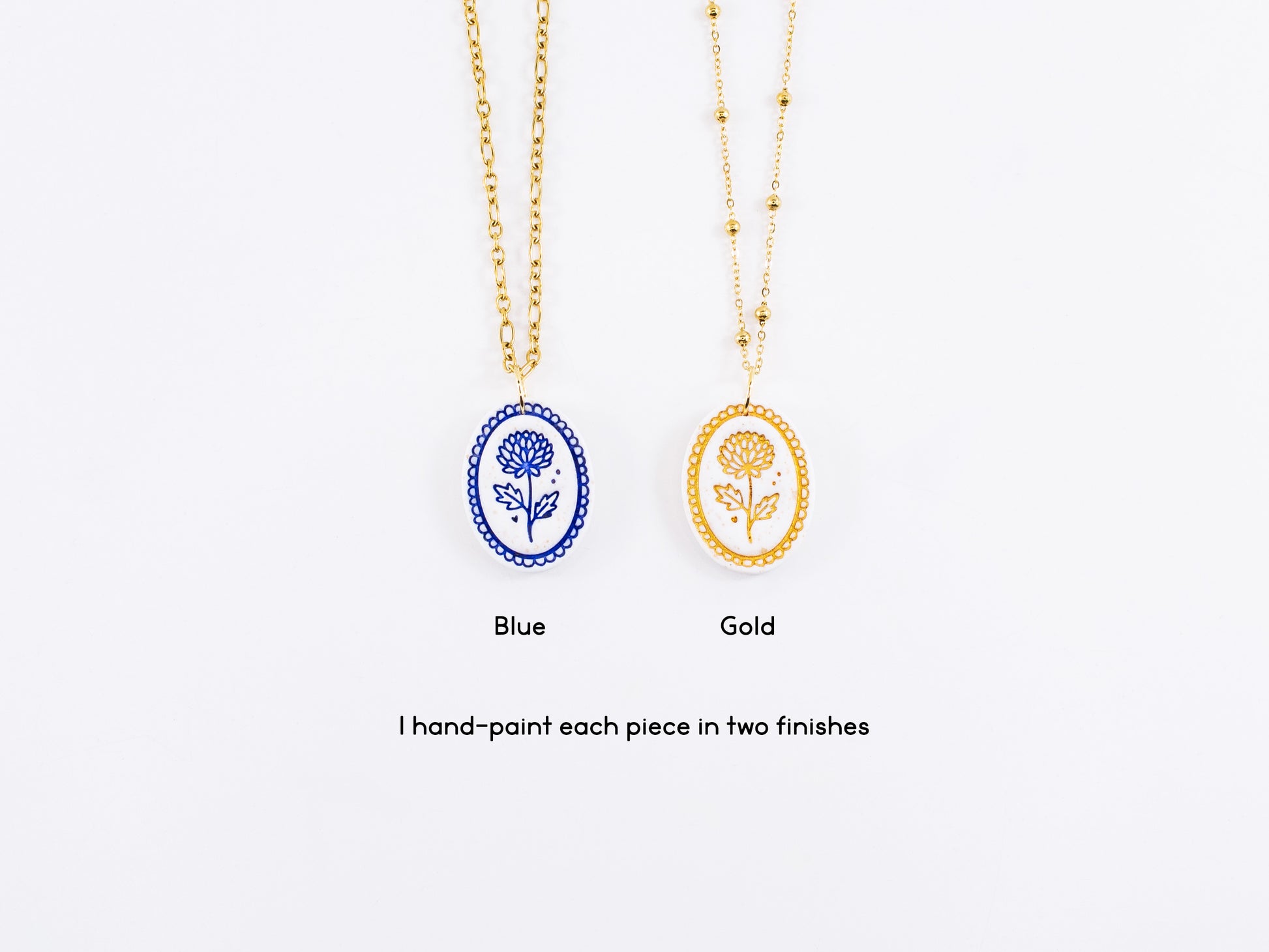 Two handmade cottagecore jewelry pendants side-by-side. The left pendant shows the November Chrysanthemum painted in cobalt blue, and the right pendant shows the same flower hand-painted in gold mica.
