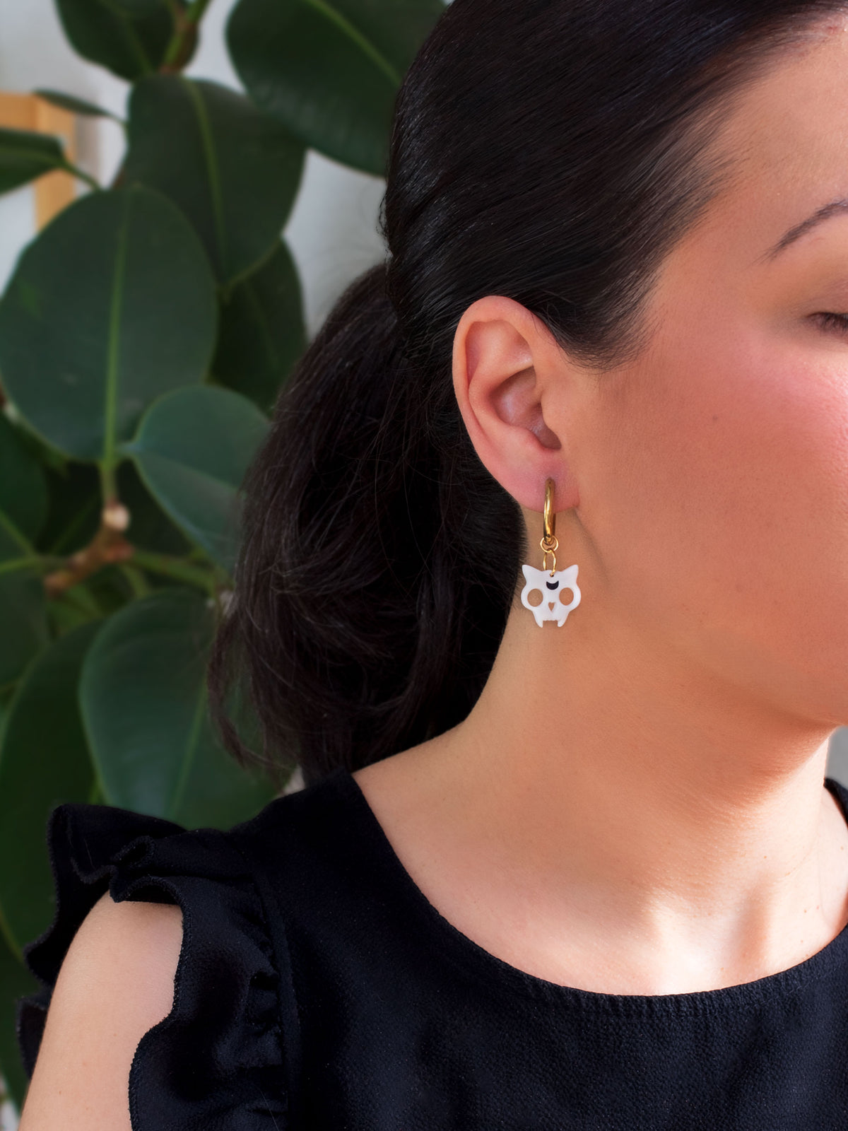 Woman wearing a spooky white cat skull charm hoop earring, part of a handmade interchangeable Halloween jewelry collection.