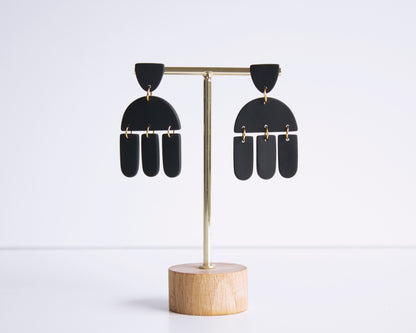 Black geometric earrings displayed on a stand, handmade with polymer clay, perfect for boho style and lightweight wear.