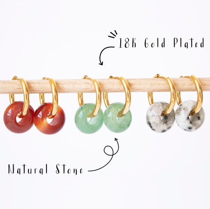Gold hoop earrings with donut gemstone charms in Aventurine, Carnelian, and Dalmatian Jasper, displayed on a wooden rod