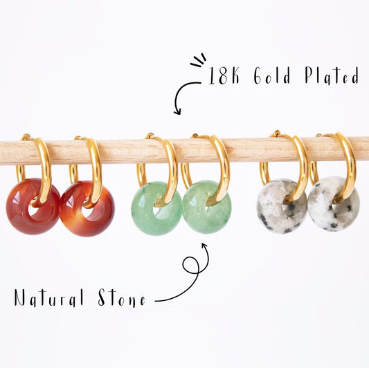 Gold hoop earrings with donut gemstone charms in Aventurine, Carnelian, and Dalmatian Jasper, displayed on a wooden rod