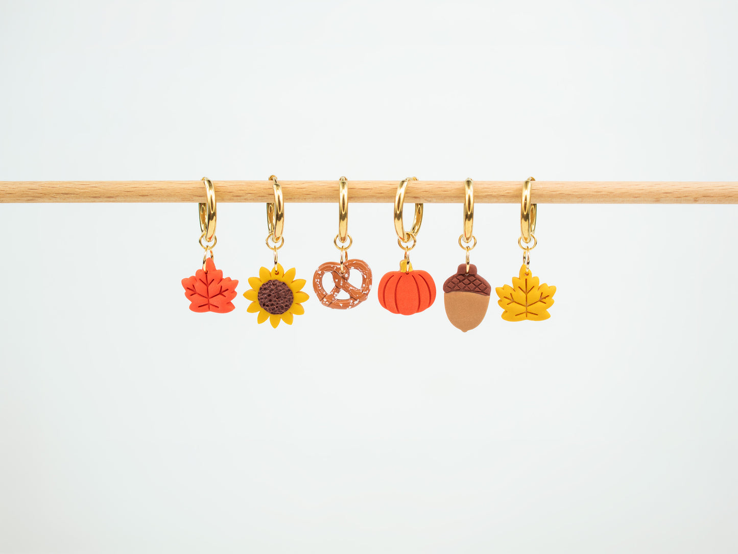 Collection of handmade autumn charm hoop earrings displaying interchangeable fall leaves, sunflower, pretzel, pumpkin, and acorn pendants.