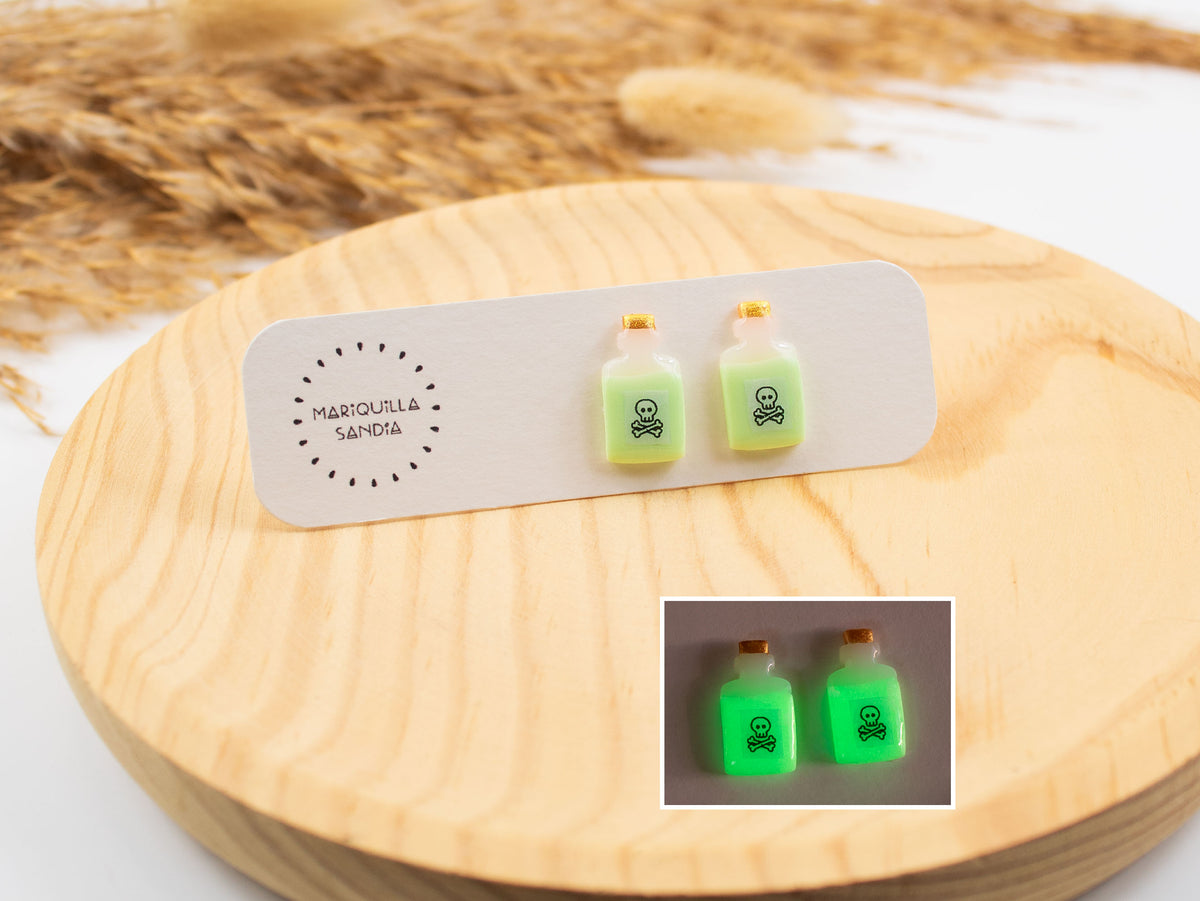 Glow in the dark potion earrings shown in daylight and glowing green at night. Handmade poison bottle studs for Halloween.