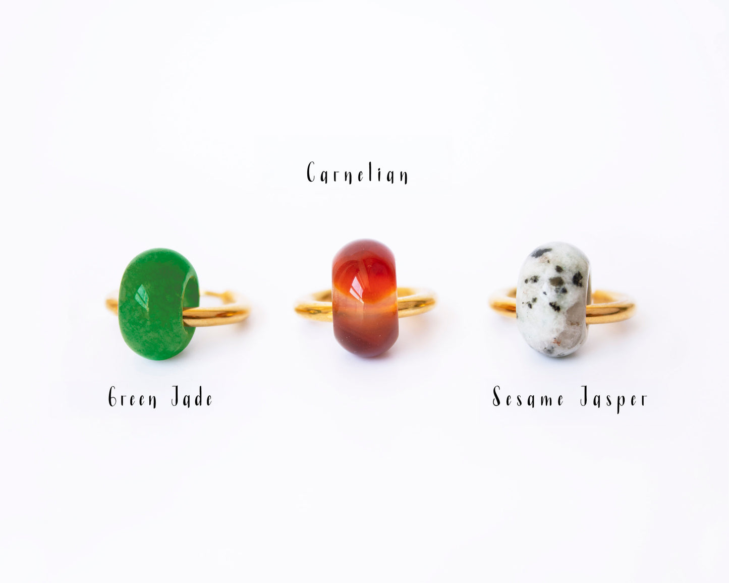 Close-up display on a white background showing single interchangeable donut stone charms—Green Jade, Carnelian, and Dalmatian Jasper—leaning against 18K gold plated hoops with labels.