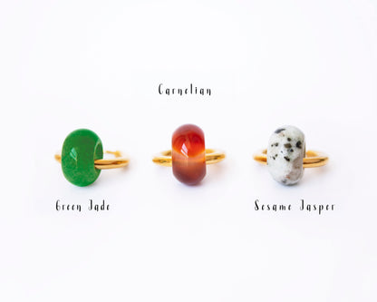 Close-up display on a white background showing single interchangeable donut stone charms—Green Jade, Carnelian, and Dalmatian Jasper—leaning against 18K gold plated hoops with labels.
